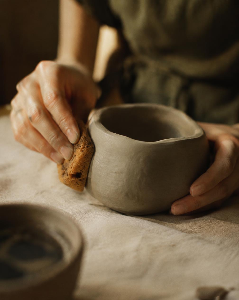 Hands smoothing a clay pot with a sponge